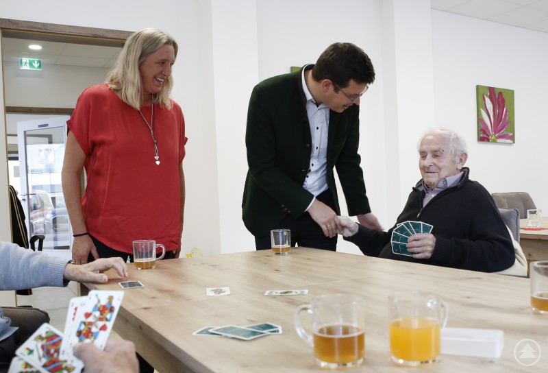 Bei der fröhlichen Montags-Schafkopfrunde lebt ein wenig die Wirtshauskultur mit früheren Spezis und einem möglichst guten Blatt wieder auf. Ludwig Groß (v.r.) begrüßte Martin Pichler freundlich in der Runde, die für ihn auch Hirntraining mit Spaß bedeutet. Corina Piller und ihr Team sorgen ständig für Abwechslung. Ein älterer Mann sitzt am Tisch und spielt Karten, während er von einem jüngeren Mann freundlich per Handschlag begrüßt wird. Eine Frau daneben lächelt, auf dem Tisch stehen Gläser mit Getränken.