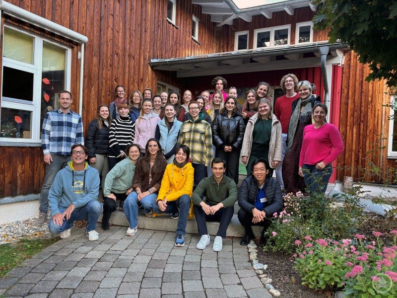 Einsatz im Kindergarten: Medizinstudierende aus dem gesamten Bundesgebiet, die derzeit ihre Famulatur in Freyung-Grafenau absolvieren, mit den Unterstützern und Organisatoren der Maßnahme: René Kurtz von der Gesundheitsregion Plus FRG (2. Reihe links außen), Regionalmanager Stefan Schuster (1. Reihe links außen), stellvertretende Kindergartenleiterin Monika Fuchs (2. Reihe rechts außen) und Elternbeiratsvorsitzende Carolin Schuster (vordere Reihe 3. von links). Eine Gruppe von etwa 30 Personen steht vor einem Holzgebäude. Es handelt sich um Studierende, Projektbeteiligte und Betreuende, die gemeinsam für ein Gruppenfoto posieren.