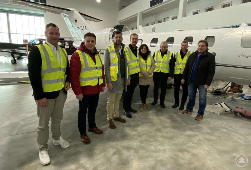 Acht Personen in Sicherheitswesten stehen in einer Flugzeughalle vor einem Gesch&auml;ftsreiseflugzeug, das Flugzeug ist seitlich zu sehen.