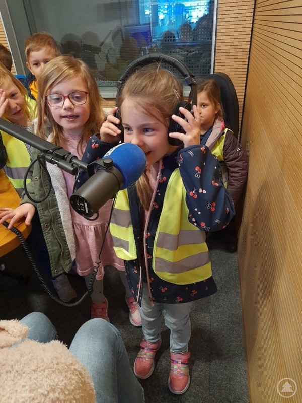 Leni hatte keine Angst vor dem Mikrofon von Unser Radio. Die Vorschulkinder aus Schönberg erlebten die Radioproduktion hautnah. Ein Mädchen trägt Kopfhörer und spricht in ein Mikrofon, während andere Kinder neugierig zusehen.