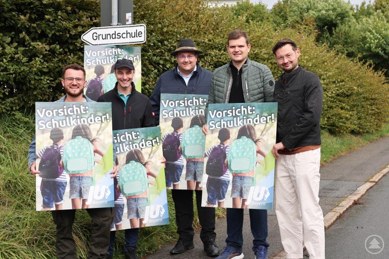 Brachten entlang der Hauptzufahrtswege zum Schulzentrum auch heuer wieder Plakate mit der Aufschrift „Vorsicht: Schulkinder!“ an: (v. li. n. re.) Matthias Kerschbaum, stellv. Ortsvorsitzender Dr.-Ing. Sebastian Weber, Ortsvorsitzender Christoph Weishäupl, Martin Höppler und Rainer Jungwirth. Fünf junge Männer stehen an einer Straße vor einem Schild zur Grundschule und halten Plakate mit der Aufschrift „Vorsicht: Schulkinder!“ in den Händen.