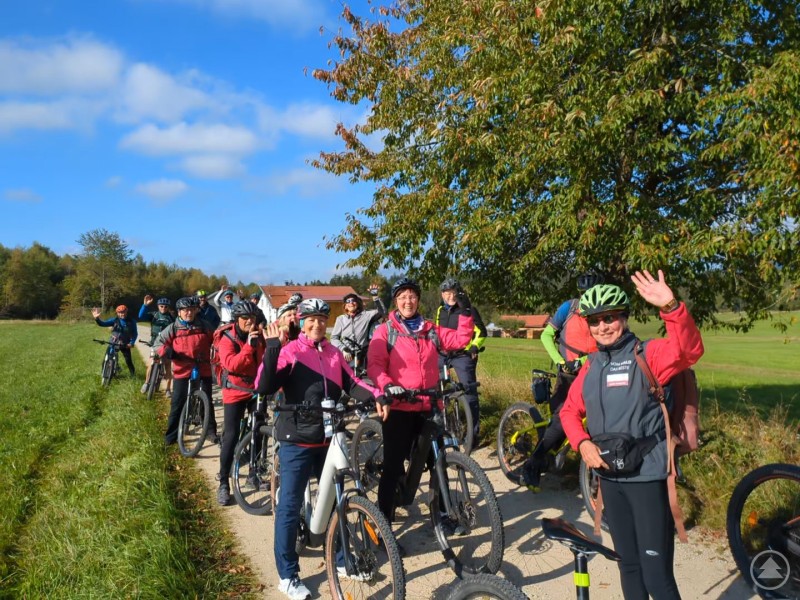 Gute Stimmung unterwegs: Über 100 Teilnehmer genossen die sportlich-kulinarische Tour. Mehrere Radfahrer stehen lachend und winkend auf einem Feldweg zwischen grünen Wiesen.
