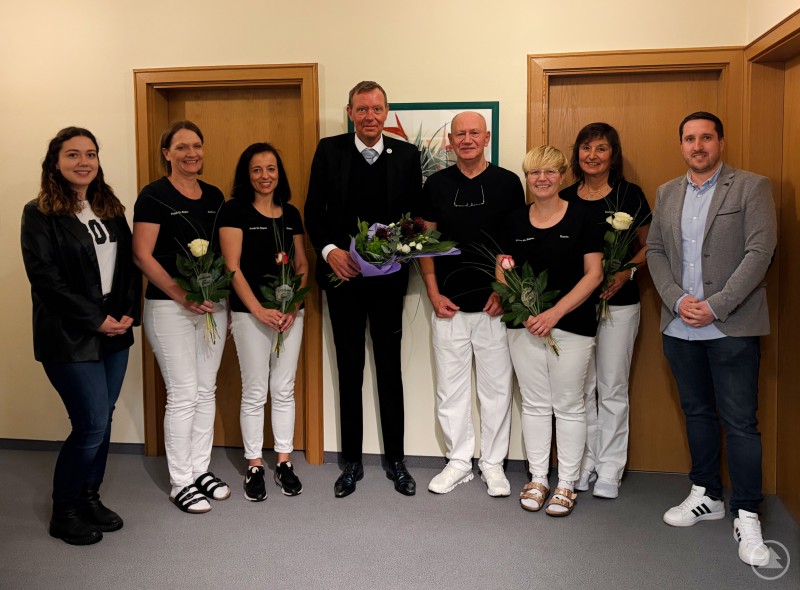 Das Praxisteam von Dr. Franz Zoltan Bogner gemeinsam mit Vertretern des Facharztzentrums Am Goldenen Steig gGmbH bei der offiziellen Bekanntgabe der Übernahme. Gruppenfoto in einem Praxisraum mit mehreren Mitarbeiterinnen der gynäkologischen Praxis, Dr. Franz Zoltan Bogner in der Mitte sowie weiteren Beteiligten. Alle stehen nebeneinander, einige halten Blumen in den Händen.