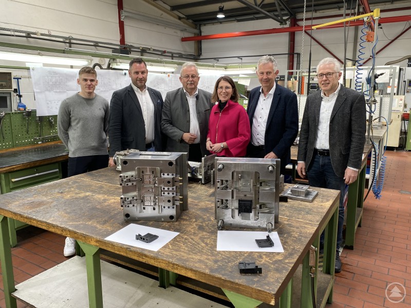 Richard Buchner (kaufmännischer Leiter), Helmut Hiendl (Geschäftsführer), Bürgermeisterin Andrea Probst, Landrat Josef Laumer, Wirtschaftsreferent Martin Köck und Dominik Anker (von links) in den Produktionsräumen der Firma in Bogen/Furth. Das Bild zeigt eine Gruppe von sechs Personen bei einem Firmenbesuch in einem metallverarbeitenden Betrieb – vermutlich bei der Firma Hiendl. In einer Werkhalle stehen die Gäste um einen Arbeitstisch, auf dem präzise gefertigte Metallformen und Bauteile präsentiert werden. Die Umgebung ist sauber und professionell, im Hintergrund sind Maschinen, Werkzeuge und technische Zeichnungen sichtbar. Die Personen wirken interessiert und freundlich – es dürfte sich um eine Unternehmensführung oder einen Austausch zwischen Wirtschaft und Politik handeln. Besonders auffällig ist die Frau in pinkem Blazer, was auf eine offizielle Funktion oder besonderen Besuch hindeuten könnte.