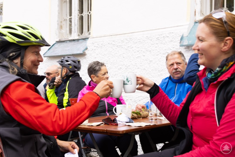 Bei den Genuss-Stationen standen neben kulinarischen Spezialitäten auch gemütliche Pausen auf dem Programm. Zwei Frauen im Radler-Outfit stoßen mit Kaffeetassen an, während andere Teilnehmer am Tisch sitzen..jpg