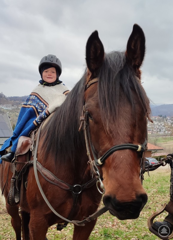Ein kleines Kind sitzt warm eingepackt auf einem Pferd und blickt in die Kamera.