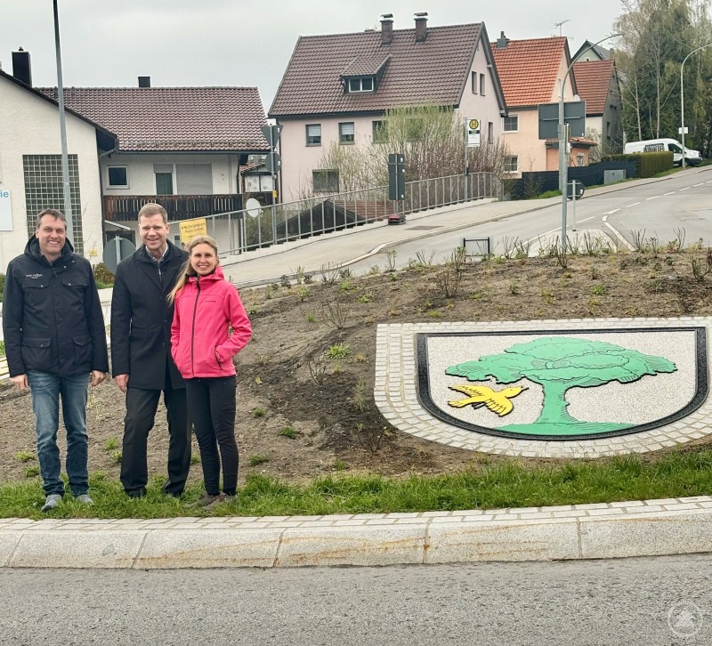 Bürgermeister Dr. Olaf Heinrich, Kreisfachberaterin Lena Fröhler und Vertreter des Bauamts beim Ortstermin am neu bepflanzten Kreisel im Aufeld. Drei Personen stehen an einem neu bepflanzten Kreisverkehr mit Wappen und betrachten die angelegte Grünfläche.