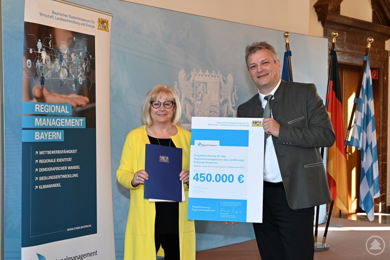 Wirtschaftsstaatssekretär Roland Weigert übergibt Freyung-Grafenaus stellvertretender Landrätin Helga Weinberger den neuen Förderbescheid.