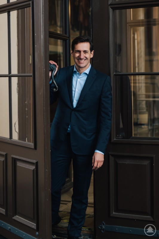 MdL Dr. Stefan Ebner freut sich über die staatliche Förderung von über 7 Mio. Euro für Bildungs- und Betreuungseinrichtungen im Landkreis Regen. Ein Mann im dunklen Anzug und hellblauen Hemd steht freundlich lächelnd in einer geöffneten braunen Tür und blickt in die Kamera. Die Umgebung wirkt repräsentativ und historisch