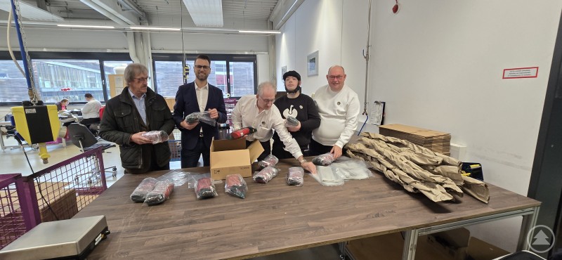 Jährlich rund 100 Millionen Teile für BMW verpacken die Caritas-Mitarbeiter v.l. Franz Hohenester und Mario Schreder, Leiter der Dienstleitersteuerung überzeugen sich von der Präzisionsarbeit Mehrere Personen stehen an einem Arbeitstisch in einer Werkstatt und verpacken Produkte. Vor ihnen liegen zahlreiche Einzelteile und Kartons bereit.