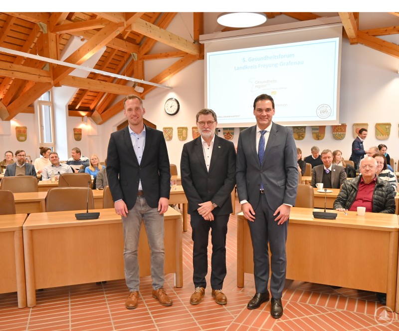 Eine spürbare Stärkung der Attraktivität des Landkreises als Gesundheitsstandort war das Thema beim fünften Gesundheitsforum, auch bei den Beiträgen von (von rechts) Landrat Sebastian Gruber, Prof. Dr. Tomas Sauer (Medizincampus, Universität Passau) und dem Geschäftsstellenleiter der GesundheitsregionPlus René Kurtz. Im Sitzungssaal eines Landratsamtes stehen drei Männer – darunter Landrat Sebastian Gruber, Prof. Dr. Tomas Sauer und René Kurtz – vor den anwesenden Gästen des 5. Gesundheitsforums Freyung-Grafenau. Im Hintergrund sind zahlreiche Teilnehmerinnen und Teilnehmer an Tischen zu sehen, an der Wand hängen regionale Wappen.