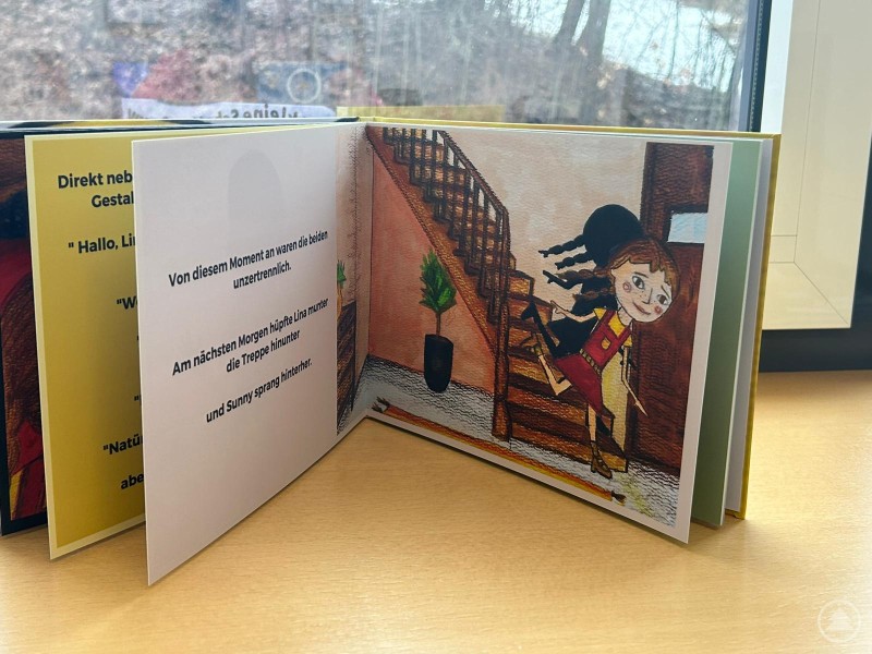 Aufgeschlagenes Kinderbuch auf einer Fensterbank. Zu sehen sind eine illustrierte Szene mit einem M&auml;dchen und seinem Schatten an einer Treppe sowie Textseiten aus dem Buch.