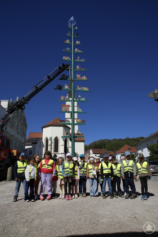 Aufgestellt! Mit Krankraft war es für den zurückgekehrten Baum in die Senkrechte gegangen. Kinder stehen vor einem aufgestellten Maibaum auf einem Dorfplatz und blicken in die Kamera.