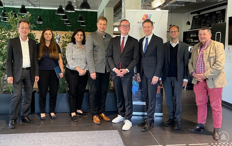 Nahmen an der Vorstands- und Beiratssitzung teil: Prof. Dr. Fritz Pörnbacher, Carmen Schnupp, Manuela Königbauer, Dr. Olaf Heinrich, Dr. Reinhard Saller, Rainer Haselbeck, Thomas Graupe und Rudi Fellner. Acht Personen stehen in Businesskleidung nebeneinander im modernen Foyer des Gründerzentrums LINK in Landshut. Im Hintergrund Pflanzen, ein Logo des Niederbayern-Forums und eine Café-Theke.