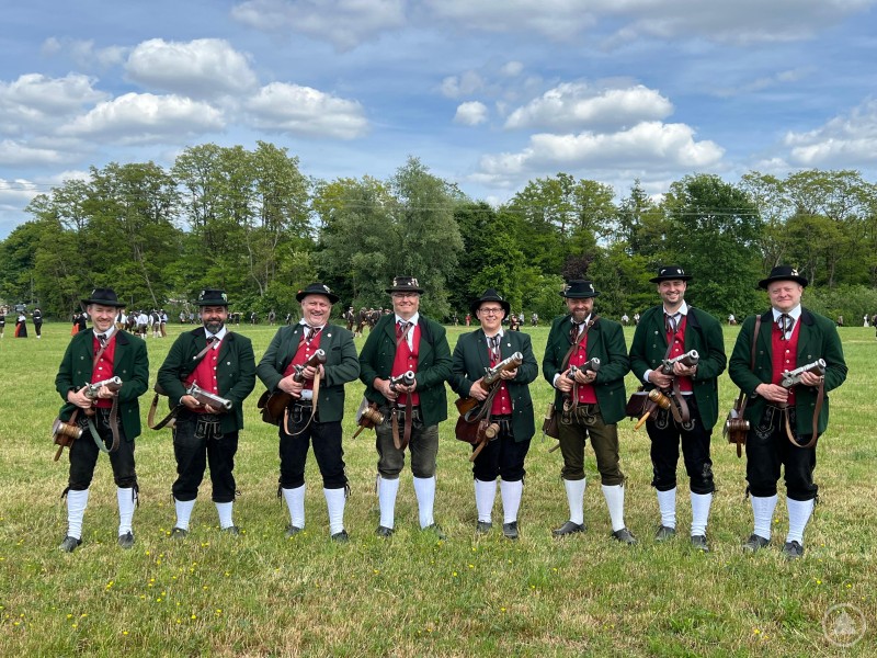 Die Böllergruppe des Musik- und Heimatvereins Haus i. Wald e.V. beim Süddeutschen Böllertreffen in Kadeltshofen. Acht Böllerschützen in traditioneller bayerischer Tracht posieren mit ihren Handböllern auf einer Wiese, im Hintergrund weitere Teilnehmer vor einer Baumkulisse.