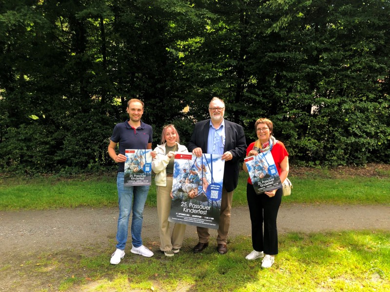 Oberbürgermeister Jürgen Dupper (2. v. r.) mit Anita Bauer (Jugendamt), Hanna Jetzinger (Zeughaus) und Tobias Waldherr (Stadtjugendring) bei der Präsentation der Plakate für das 25. Passauer Kinder- und Familienfest. Vier Personen stehen im Grünen nebeneinander und halten Plakate zum Passauer Kinder- und Familienfest. Zwei Frauen und zwei Männer lächeln in die Kamera.