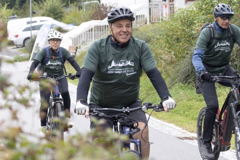 Mit Rückenwind und guter Laune bewältigten die Teilnehmer die Genussstrecke. Drei Radfahrer mit grünen Event-T-Shirts und Helmen fahren lächelnd auf einer Straße.