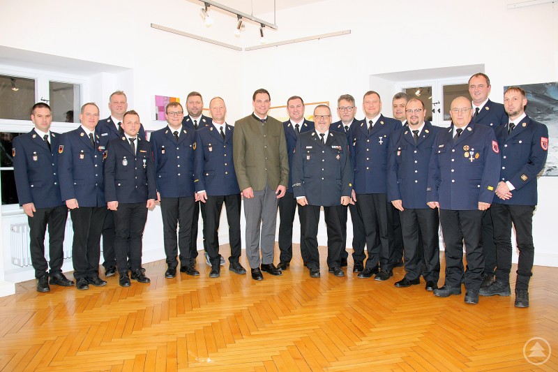 Landrat Sebastian Gruber (Mitte) mit den neuen Mitgliedern der Kreisbrandinspektion, darunter die Kreisbrandinspektoren und Kreisbrandmeister des Landkreises Freyung-Grafenau. Eine Gruppe von 16 Männern in Feuerwehr-Uniform sowie Landrat Sebastian Gruber steht gemeinsam in einem hellen Raum, alle sind für ein Gruppenfoto aufgestellt. Die Stimmung ist festlich und kameradschaftlich.