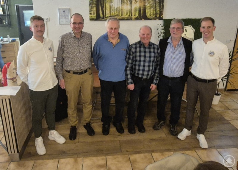 Beim TSV Spiegelau wurden langjährige Mitglieder für 25 und 60 Jahre Vereinstreue geehrt. Sechs Männer stehen nebeneinander in einem Vereinsheim, im Hintergrund hängt ein großes Bild mit Waldmotiv an der Wand.