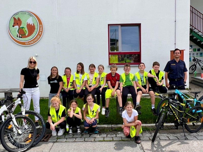 Die siegreiche 4. Klasse der Grundschule Kirchdorf mit Verkehrserzieher Maximilian Dengler nach der erfolgreichen Fahrradausbildung. Schüler der 4. Klasse der Grundschule Kirchdorf mit gelben Warnwesten, Fahrrädern und ihren Betreuern vor dem Schulgebäude. Ein Polizist und zwei Lehrerinnen stehen am Rand der Gruppe.