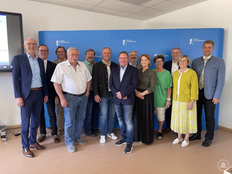 Nahmen am Genossenschaftstag 2025 teil: Albert Griebl, Bezirkspräsident für Niederbayern beim Genossenschaftsverband Bayern (v. l.), Geschäftsführer des Niederbayern Forums Dr. Reinhard Saller, Johann Luger, Bürgermeister der Gemeinde Gerzen, Joachim Walther, stv. Vorstand der Senioren-Wohnen-Mitterkirchen e. G., Max Riedl, Gründungsberater des Genossenschaftsverbands, Michael Breu, Vorstandsvorsitzender Nahwärme Rattenberg, Manfred Sperl, Vorsitzender Dorfgenossenschaft Malgersdorf, Franz Penker, Regionaldirektor im Genossenschaftsverband Bayern, Mia Goller, MdL, Bezirksrätin Hannelore Langwieser, Malgersdorfs Bürgermeister Franz Josef Weber, Anna Nagl, Bürgermeisterin der Gemeinde Falkenberg, und Bezirkstagspräsident Dr. Olaf Heinrich. Eine Gruppe von 13 Personen steht nebeneinander vor einer blauen Pressewand mit dem Logo des Bezirks Niederbayern. Alle lächeln in die Kamera, einige tragen Anzüge, andere sind leger gekleidet.