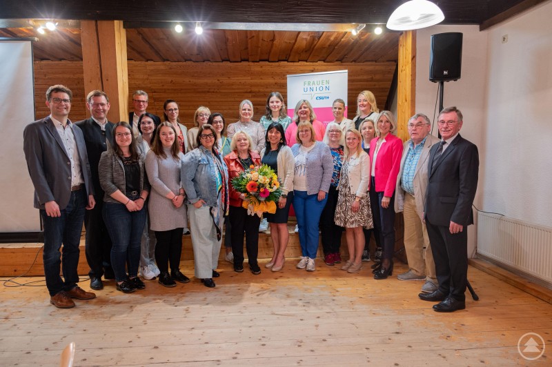 v.l. hinten: Paul Linsmeier Ortsvorsitzender CSU, Thomas Erndl MdB, Bernd Sibler Landrat, Monika Rengsberger, Beate Lausch-Bernreiter, Katharina Stündler, Sabine Wasöhrl, Melissa Achatz, Yvonne Pletl-Schäfer, Bernadette Batzlsperger, Sabrina Löffelmann-Schaß v. l. vorne: Selina Vandieken, Julia Griesbauer, Sabrina Edmeier, Dr. Ila Schnabel, Margret Tuchen, Petra Schwankl, Cathrina Baumgartner, Theresia Wellner, Manuela Staudinger, Maria Maier, Renate Wasmeier Bezirksrätin, Hermann Hilmer Senioren-Union, Barthl Kalb MdB a. D. Das Bild zeigt eine große Gruppe von Frauen und Männern bei einer Veranstaltung der Frauen-Union der CSU. Im Zentrum der Gruppe steht eine Frau mit einem Blumenstrauß, was auf eine Ehrung oder einen besonderen Anlass hindeutet. Die Personen stehen vor einem Banner mit dem Logo der Frauen-Union. Der Raum hat eine warme Holzoptik, die Atmosphäre wirkt freundlich und feierlich – vermutlich handelt es sich um eine Mitgliederversammlung, Jubiläumsfeier oder eine Vorstandswahl.