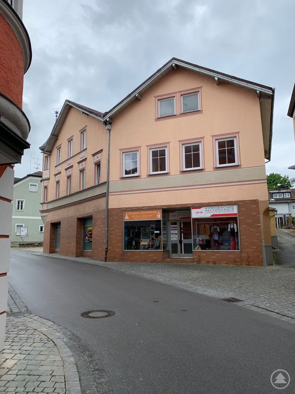 Die Aidenbacher Kleiderkammer in der Ludwigstraße 6 öffnet am 26. Oktober zum Kleidertausch und Tag der offenen Tür. Ein zweigeschossiges, hellorangefarbenes Gebäude an einer gepflasterten Straße. Im Erdgeschoss befinden sich zwei Geschäfte mit großen Schaufenstern, darunter die „Aidenbacher Helferkreis-Kleiderkammer“. Das Haus liegt an einer leichten Kurve in ruhiger Ortslage.