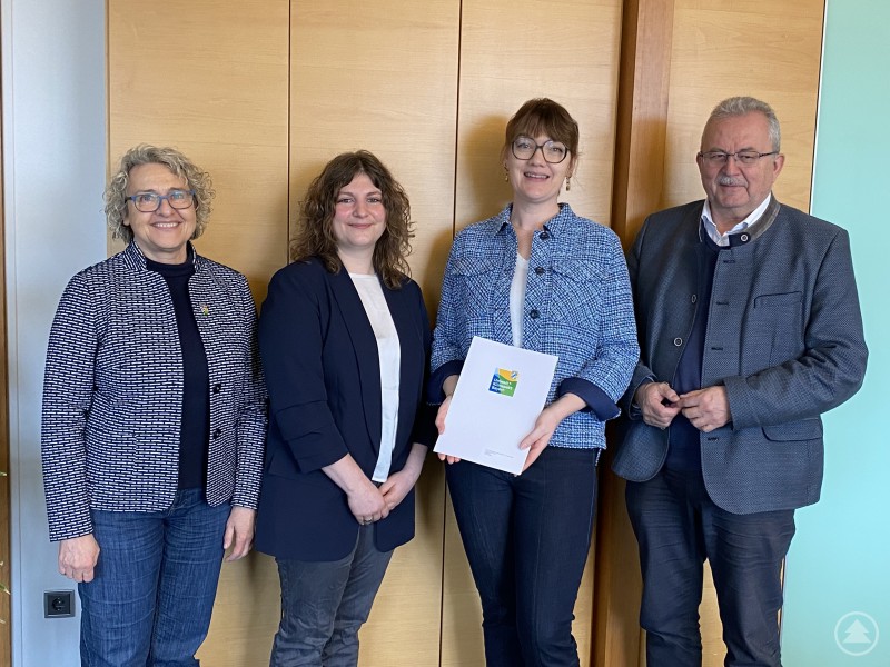 Christine Hammerschick Bürgermeisterin Steinach, Johanna Aschenbrenner, Dr. Stephanie Torkler, Landrat Josef Laumer von links bei der Übergabe der Urkunde im Büro des Landrats. Vier Personen stehen vor einer Holztür in einem Büro. Zwei Frauen halten eine Urkunde mit dem Logo des Umwelt- und Klimapakts Bayern, daneben stehen eine weitere Frau sowie ein Mann im Anzug.