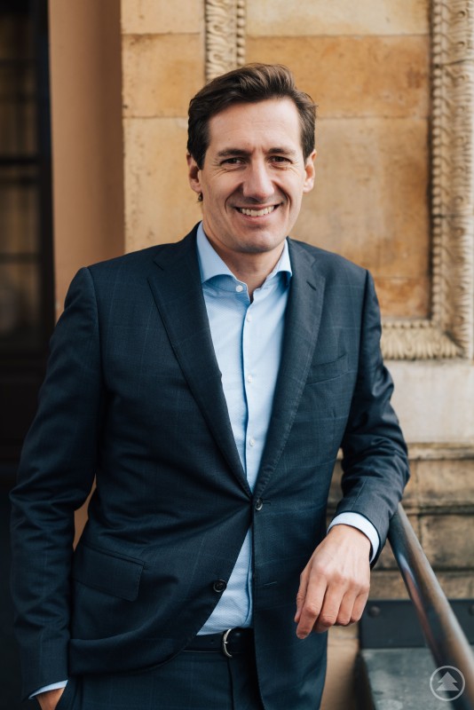 Dr. Stefan Ebner ist der neue digitalpolitische Sprecher der CSU-Fraktion im Bayerischen Landtag. Ein Mann mittleren Alters mit dunklem Haar steht im Anzug und offenem Hemdkragen vor einer beigen Wand mit Zierornamenten. Er lächelt freundlich in die Kamera und stützt sich lässig auf ein Geländer.