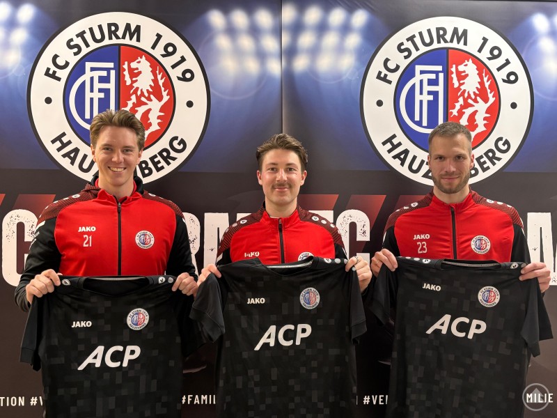 Manuel Mader, Dominik Manzenberger und Stefan Schulz bleiben dem FC Sturm Hauzenberg auch in der kommenden Saison erhalten. Drei Fußballspieler des FC Sturm Hauzenberg präsentieren neue Trikots vor einer Vereinswand mit Logo.