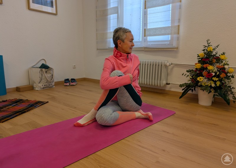 Franziska Brunner sitz auf ihrer Yogamatte und dreht sich zur&uuml;ck in eine Dehnung.