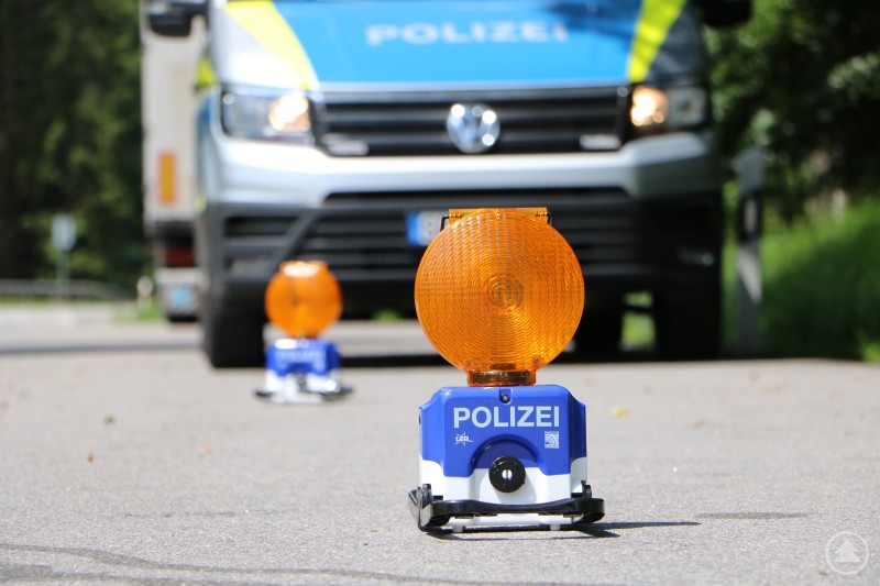 Polizeiliche Kontrollstelle im Straßenverkehr. Mobile Warnleuchten mit der Aufschrift Polizei stehen auf der Straße, im Hintergrund ist ein Polizeifahrzeug zu sehen.