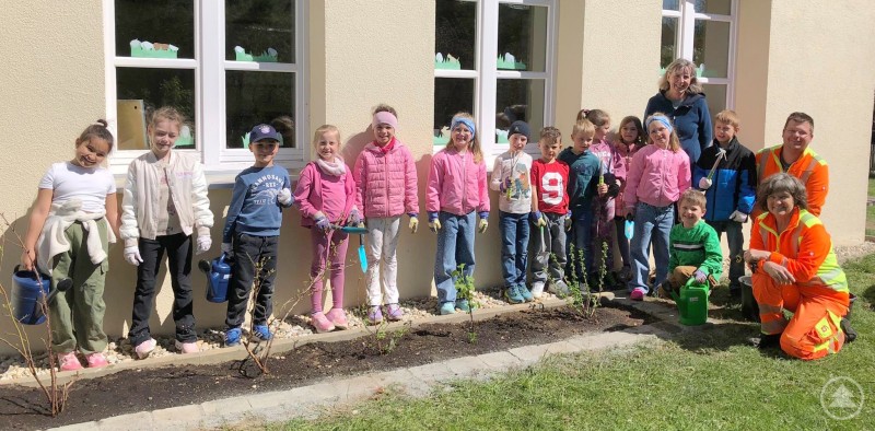 Auch im Schulgarten der Grundschule Innernzell-Schöfweg wurde von jungen Gärtnerinnen und Gärtnern fleißig gepflanzt. Eine Gruppe von Kindern steht mit Gartengeräten und Pflanzen vor einem frisch bepflanzten Beet an einer Schule.