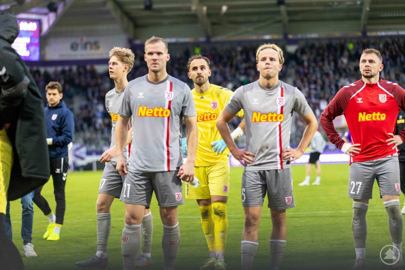 Spieler des SSV Jahn Regensburg blicken nach dem Spiel enttäuscht, während im Hintergrund Fans zu sehen sind.