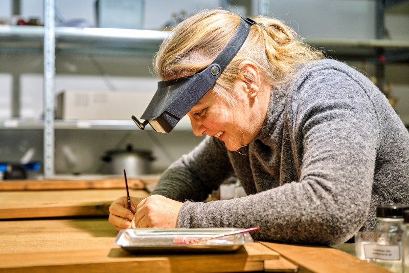 Restaurierung im Oberhausmuseum. Eine Restauratorin arbeitet mit Lupenbrille konzentriert an einem feinen Kunstobjekt in einer Werkstatt des Museums.