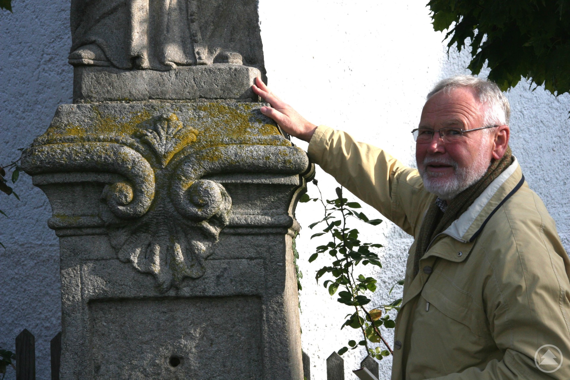 Historiker und Heimatforscher Paul Praxl hat am 17. Mai Geburtstag und wird 90 Jahre alt. Er ist u.a. ein profunder Kenner auserlesener Steinmetzkunst aus heimischem Granit. Paul Praxl, ein älterer Herr mit grauem Haar und Bart, trägt eine beige Jacke und steht neben einem historischen Steinsockel. Mit der Hand zeigt er auf Details der kunstvollen Steinmetzarbeit.