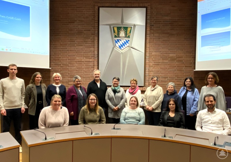 Die Teilnehmerinnen gemeinsam mit den Organisatoren und Referenten im Sitzungssaal des Landratsamtes. Gruppenfoto der Teilnehmenden der Informationsveranstaltung für Kindertagespflegepersonen im Sitzungssaal des Landratsamtes Straubing-Bogen. Mehrere Personen stehen und sitzen vor dem Wappen des Landkreises.