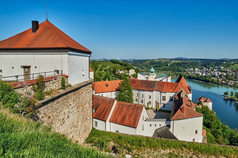 Die Veste Oberhaus in Passau lädt am Internationalen Museumstag zu spannenden Einblicken hinter die Kulissen ein. Blick über die Veste Oberhaus in Passau mit historischen Gebäuden und der Donau im Hintergrund bei sonnigem Wetter.