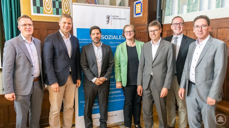 Alexander Seidl, Leiter der Bezirkssozialverwaltung, Bezirkstagspräsident Dr. Olaf Heinrich, Jakob Wild, Bayerischer Bezirketag, Evelyn Weilmeier, Bundesagentur für Arbeit, Reinhard Grepmair, Bayerischer Bezirketag, Dr. Reinhard Saller, Geschäftsführer Niederbayern-Forum e. V., Thomas Hofbrückl, ARGE Behindertenhilfe Niederbayern Eine Gruppe von sieben Personen steht vor einem Banner des Bezirks Niederbayern. Sie lächeln in die Kamera und repräsentieren verschiedene Organisationen der Eingliederungshilfe.