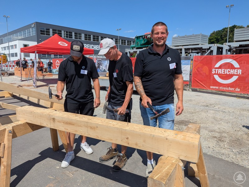 Drei Mitarbeiter der Zimmerei-Abteilung von STREICHER schlagen Nägel in ein Holzbrett