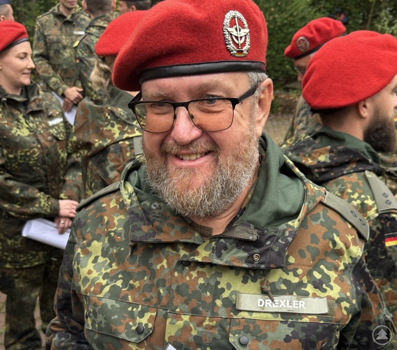 Porträtaufnahme von Gerhard Drexler in Uniform mit rotem Barett und Namensschild, umgeben von Kameraden.