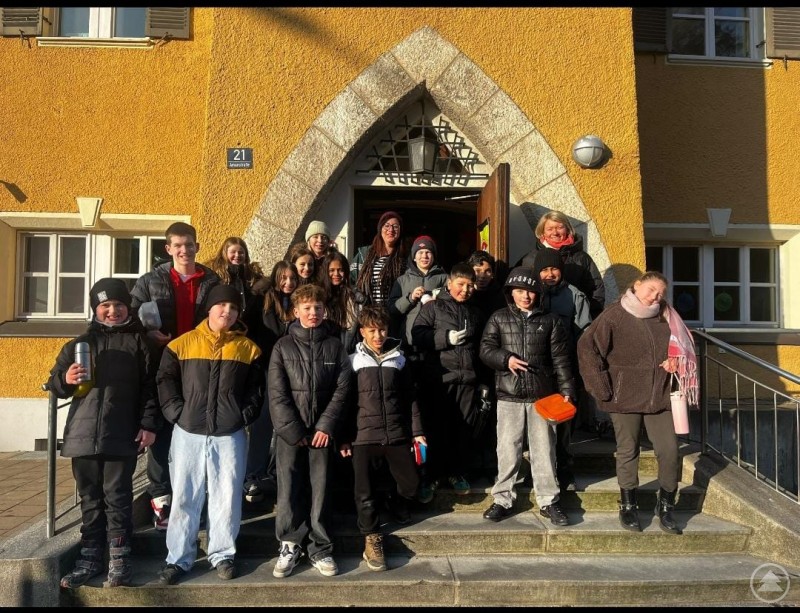 Die Schulklasse mit ihren Beteuern vor dem Jugendcenter 4You Eine Schulklasse mit Jugendlichen und Betreuungspersonen steht vor dem Eingang des Jugendcenters 4You in Deggendorf. Die Gruppe posiert auf einer Treppe vor einem gelben Gebäude mit Rundbogenportal.