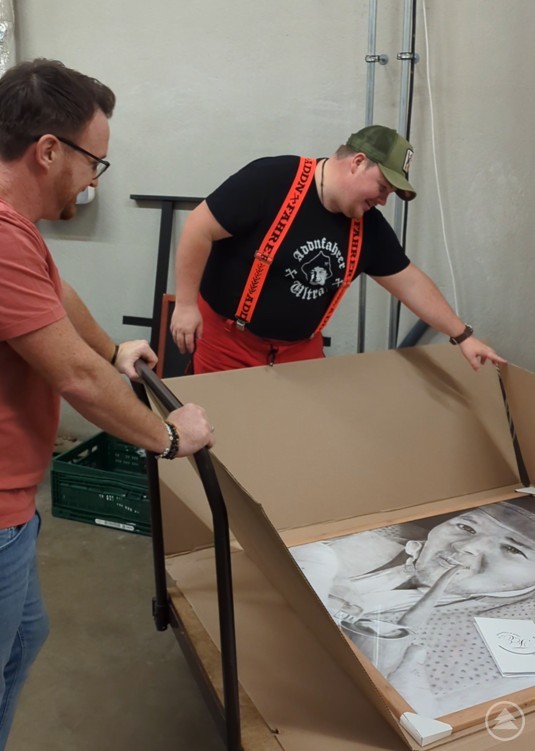 Florian Eibl und der Addnfahrer verpacken das gerahmte Portrait f&uuml;r den Transport.
