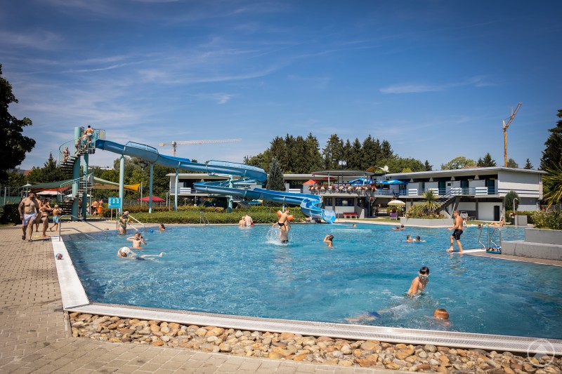 Belebtes Freibad mit vielen Badeg&auml;sten im Wasser und gro&szlig;er Rutsche im Hintergrund
