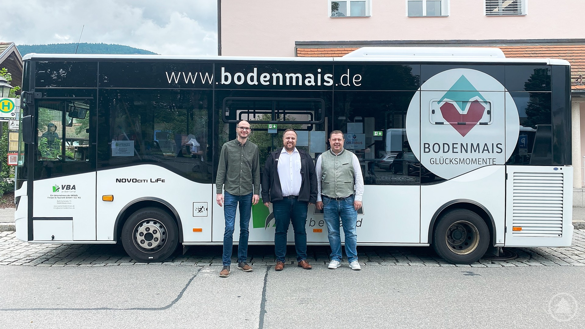 Erfreut über die erste Auswertung der Fahrgastzahlen (v.l.): BTM-Geschäftsführer Tobias Wolf, Busunternehmer Benedikt Wenzl und Bürgermeister Michael Adam. Drei Männer stehen lächelnd vor einem weißen Linienbus mit der Aufschrift „www.bodenmais.de“ und dem Logo „Bodenmais Glücksmomente“, im Hintergrund ein Gebäude mit rosa Fassade.