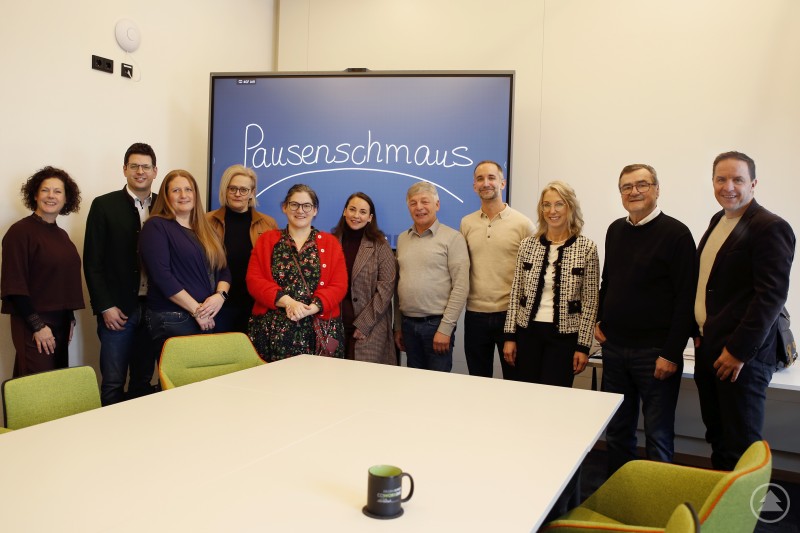 Sie machen sich stark für eine flotte App zur Versorgung der Kids mit frischer Pausenpower: Bettina Marjanovic v.l., Martin Pichler BGM Markt Schönberg, Carina Bredl, Carolin Garhammer, Carolin Pecho BGMin Ringelai, Lena Schandra Ilzer Land, Leo Meier BGM Röhrnbach, Julian Scheuchenzuber, Michaela Gampe, Josef Kern BGM Innernzell und Gerhard Poschinger BGM Perlesreut. Vertreter mehrerer Gemeinden stehen gemeinsam in einem Besprechungsraum vor einem Bildschirm mit der Aufschrift Pausenschmaus.