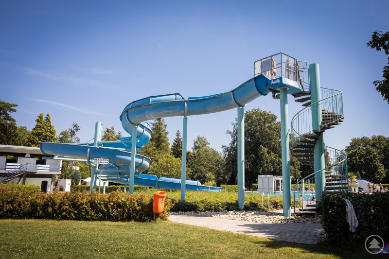Gro&szlig;e blaue Wasserrutsche mit Treppenturm in einem Freibad an einem sonnigen Tag