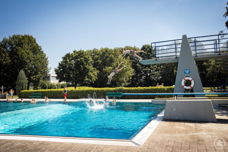 Kinder springen von einem Sprungturm in ein Schwimmbecken im Freibad