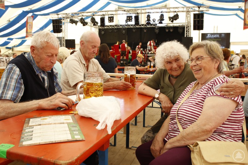 Tisch 347 war nicht dessen Nummer sondern die Zahl der Jahre, die die Senioren schon mit guter Stimmung hinter sich gebracht haben. Vier Seniorinnen und Senioren sitzen lachend an einem Biertisch mit Maßkrügen im Festzelt.
