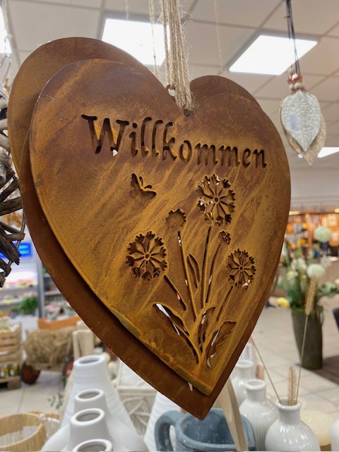 Mit Liebe zum Detail - der Dorfladen Haselbach heißt seine Kundinnen und Kunden herzlich willkommen. Ein dekoratives Metallschild in Herzform mit der Aufschrift „Willkommen“ hängt zwischen liebevoll arrangierten Dekoartikeln im Laden. Die warme Gestaltung vermittelt ein einladendes Gefühl und unterstreicht das besondere Ambiente des Dorfladens.